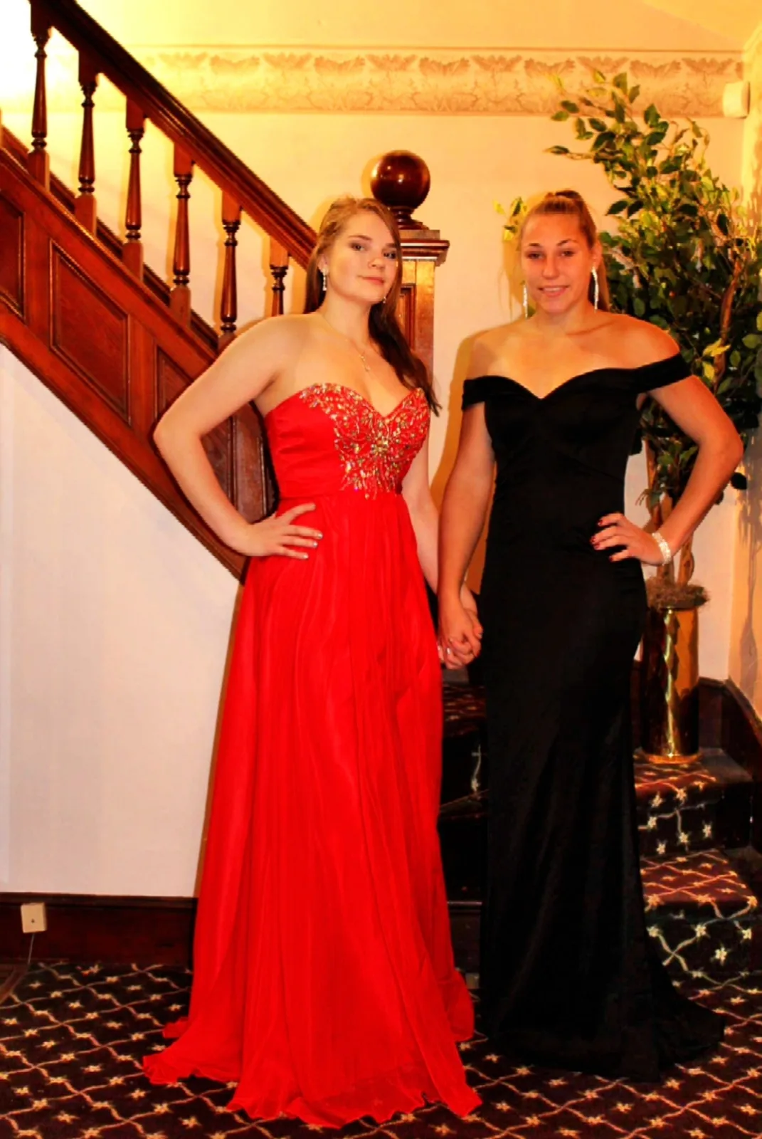 Two prom customers in a red gown and a black gown on the staircase at Maria Christine's