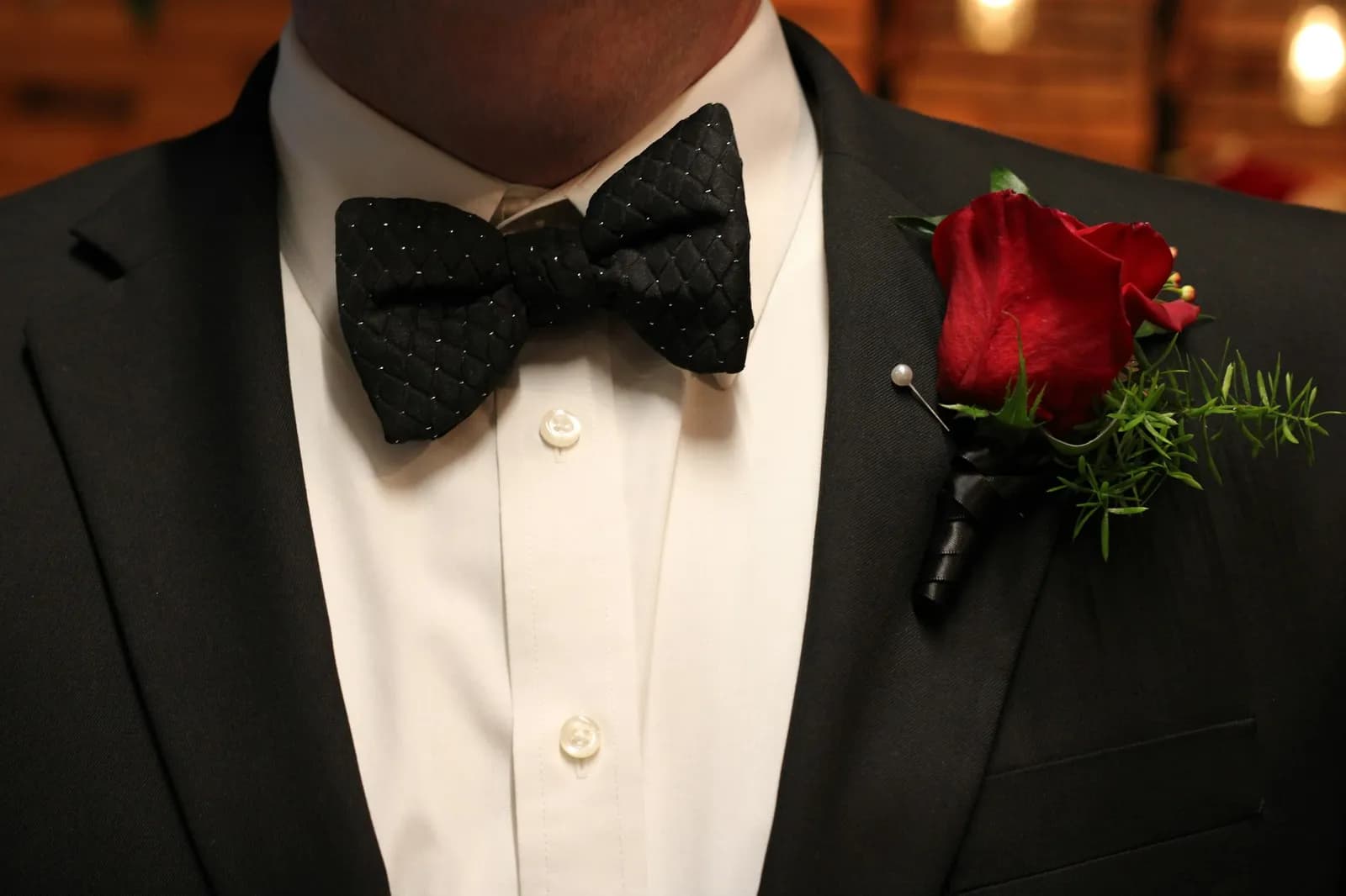 A black bow tie and a red rose boutonniere on a tuxedo
