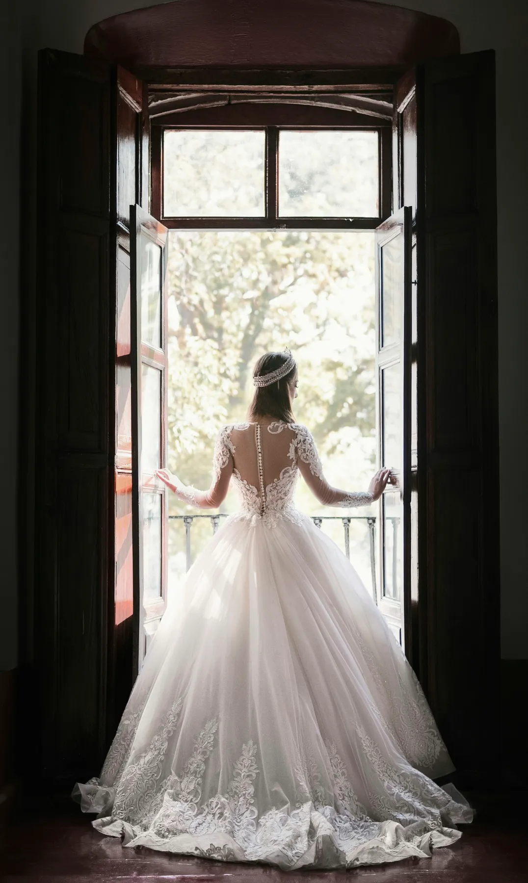 A bride in a lace ball gown standing in a tall open doorway, seen from behind