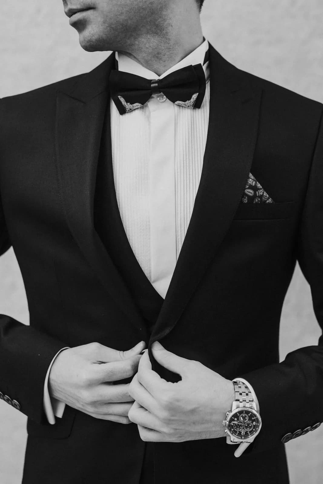 A man in a black tuxedo and bow tie buttoning his jacket